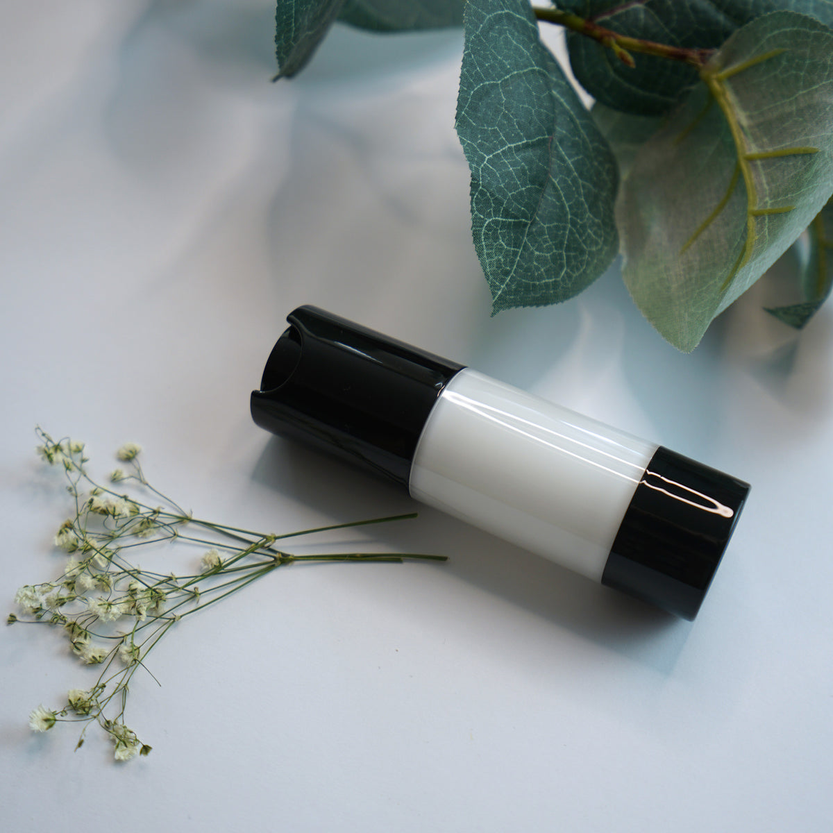White moisturizer bottle with black cap beside green leaves and delicate flowers